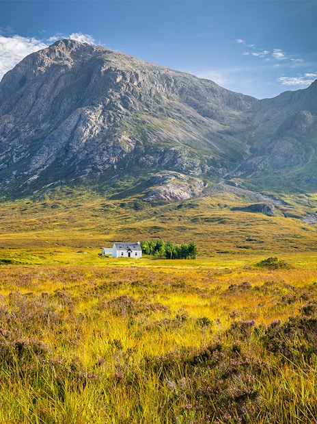 Remote hut amidst lush greenery and mountains in Glencoe, Scotland.