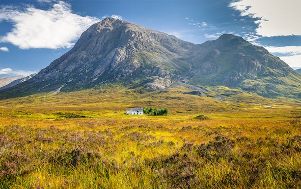 Remote hut amidst lush greenery and mountains in Glencoe, Scotland.