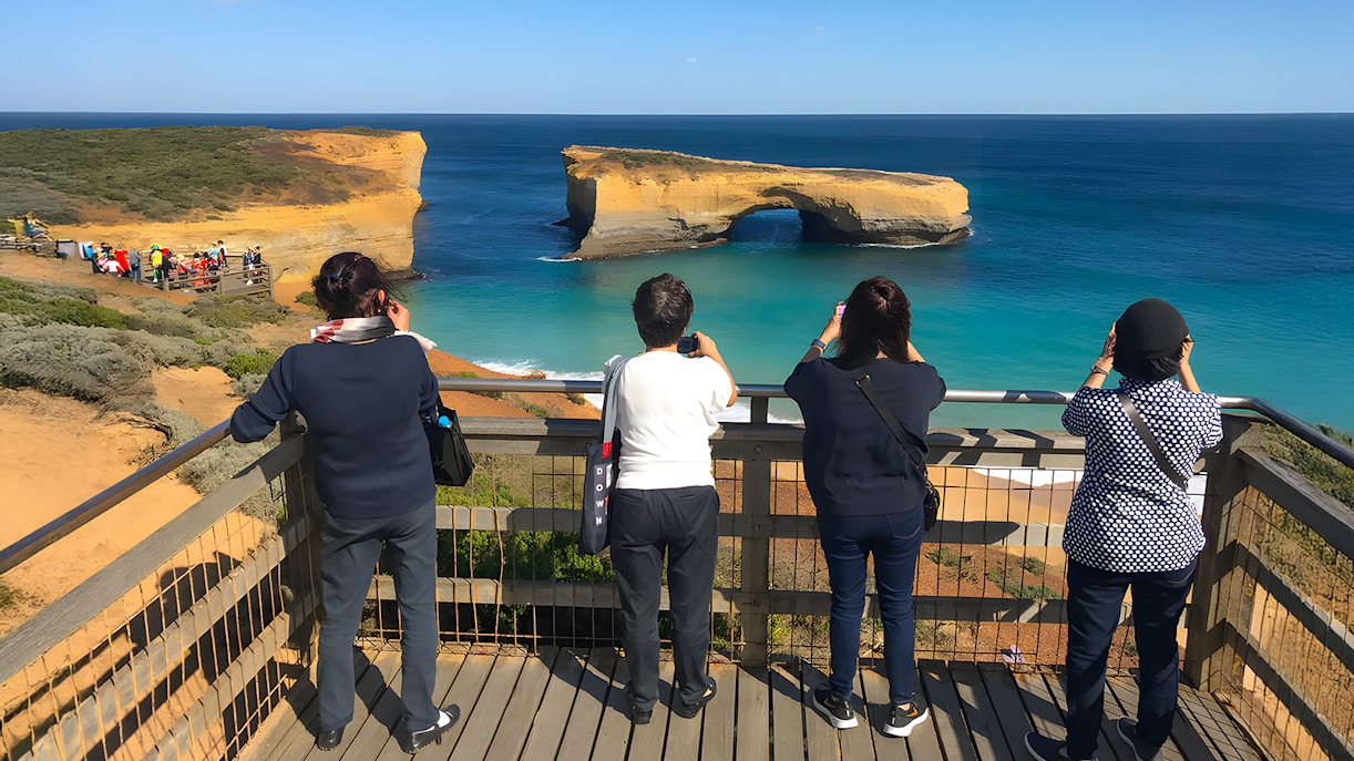 Tourists at a viewpoint overlooking the Great Ocean Road during sunset.