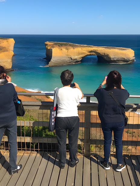 Tourists at a viewpoint capturing the scenic view of the Great Ocean Road's coastal arch formation.