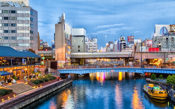 Tombori River Cruise boat on Dotonbori Canal in Osaka, Japan, with cityscape and illuminated buildings.
