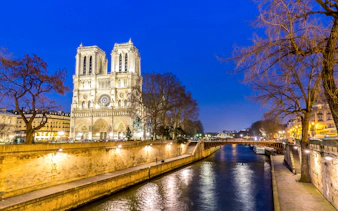 Notre-Dame Cathedral illuminated at night by the Seine River in Paris.