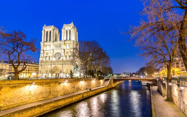 Notre-Dame Cathedral illuminated at night by the Seine River in Paris.