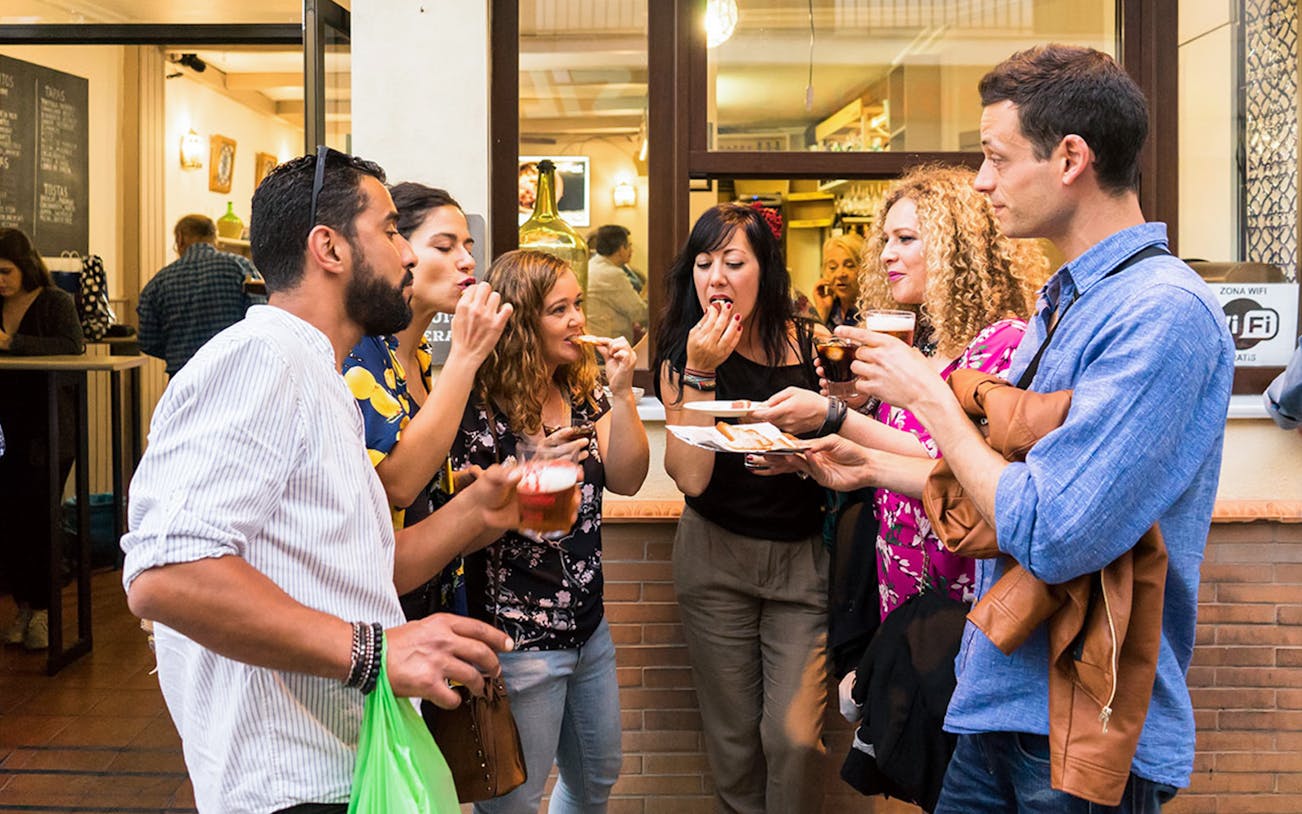 Group enjoying tapas and drinks outside a bar in Seville during a tasting tour.