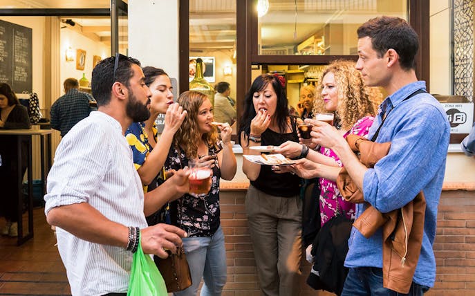 Group enjoying tapas and drinks outside a bar in Seville during a tasting tour.