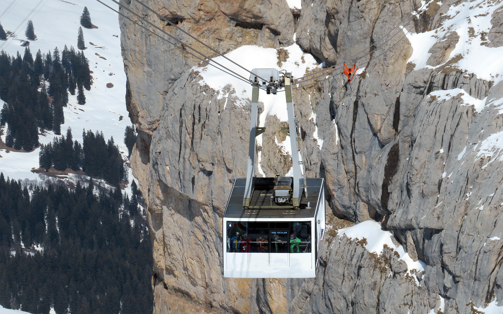Eine Seilbahn schwebt über einer Schneelandschaft mit Tannen und Bergen