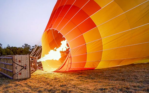 Hot air balloon inflating with flame on grassy field for luxury experience.
