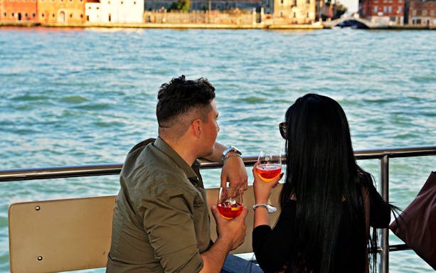 Couple enjoying drinks on a boat during the Guided Sunset Panoramic Tour in Venice.