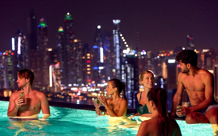 Tourists enjoying Aura Sky Pool with Dubai skyline at night.