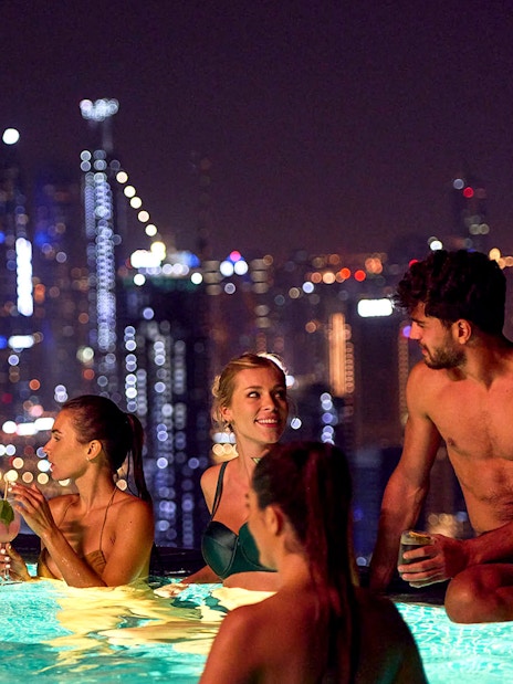 Tourists enjoying Aura Sky Pool with Dubai skyline at night.