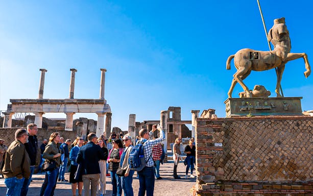 Centaur di Igor Mitoraj sculpture in Pompeii, Italy, with ancient ruins in the background.