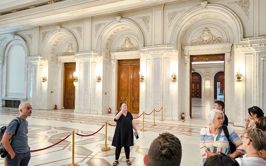 Guide leading a tour inside the ornate interior of the Palace of Parliament.