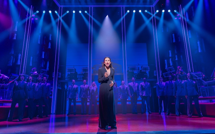 Stage performance of Chess Broadway show with lead singer and ensemble under blue lights.