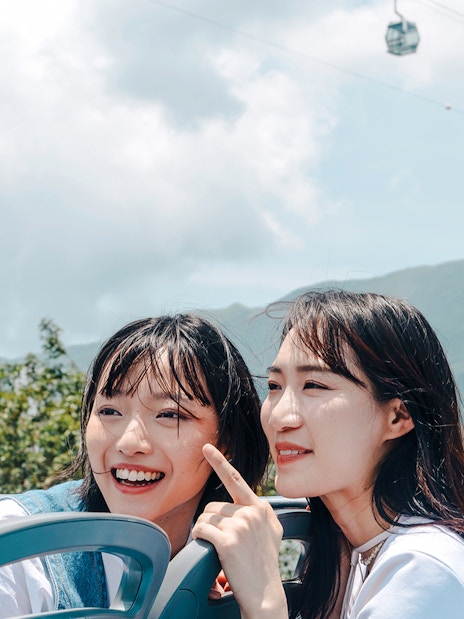 Tourists enjoying Lantau Island view from hop-on hop-off bus with cable cars above.
