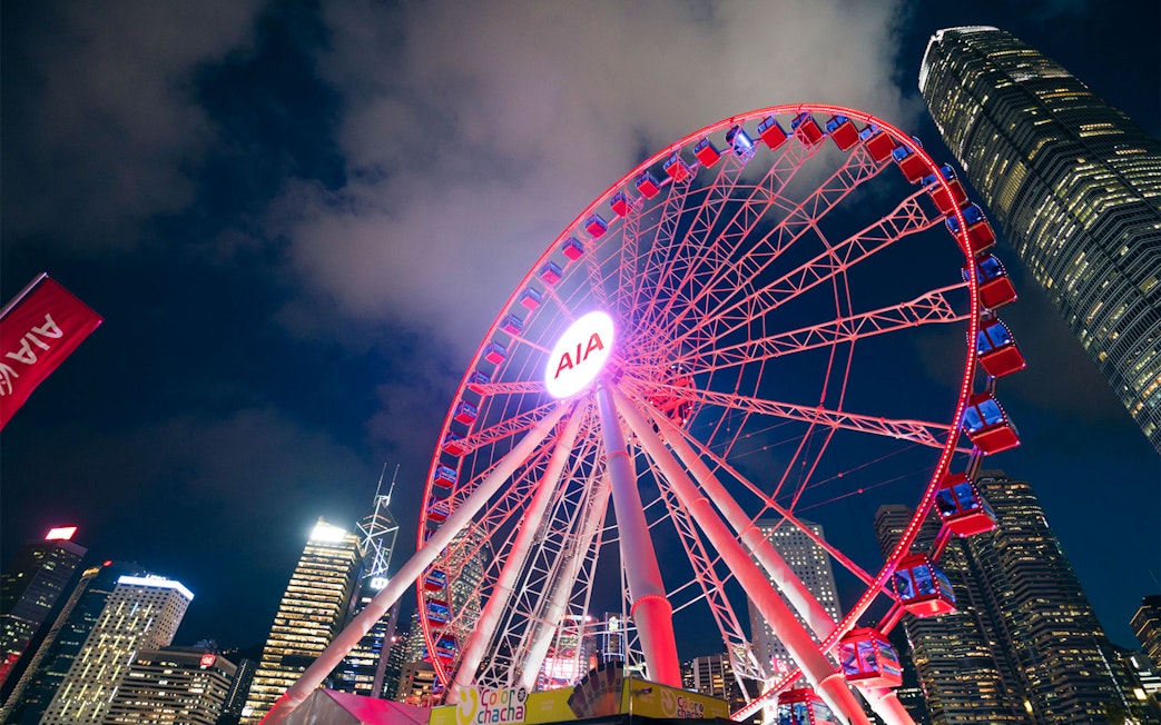 Hong Kong Observation Wheel illuminated at night with city skyline.