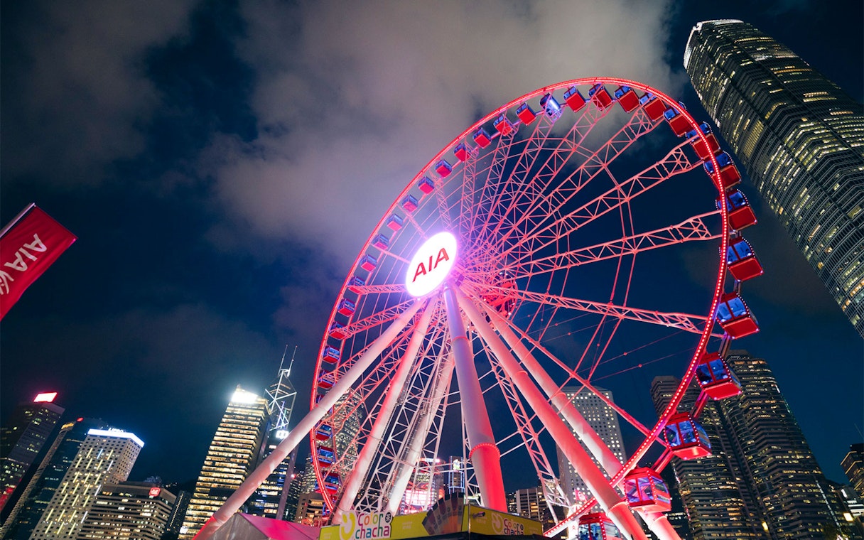 Hong Kong Observation Wheel illuminated at night with city skyline.