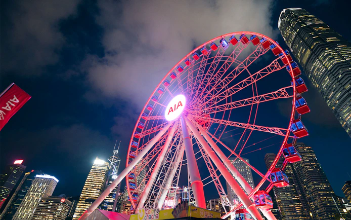 Hong Kong Observation Wheel illuminated at night with city skyline.