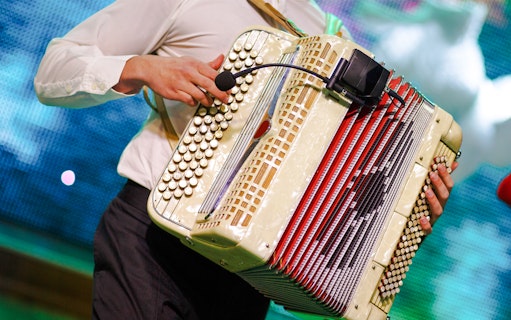 Musician playing an accordion on stage with a microphone attached.
