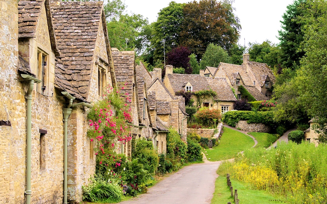 Arlington Row cottages in Bibury, Cotswolds, with stone walls and lush greenery.