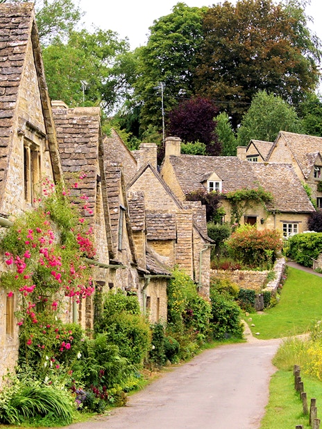Arlington Row cottages in Bibury, Cotswolds, with stone walls and lush greenery.