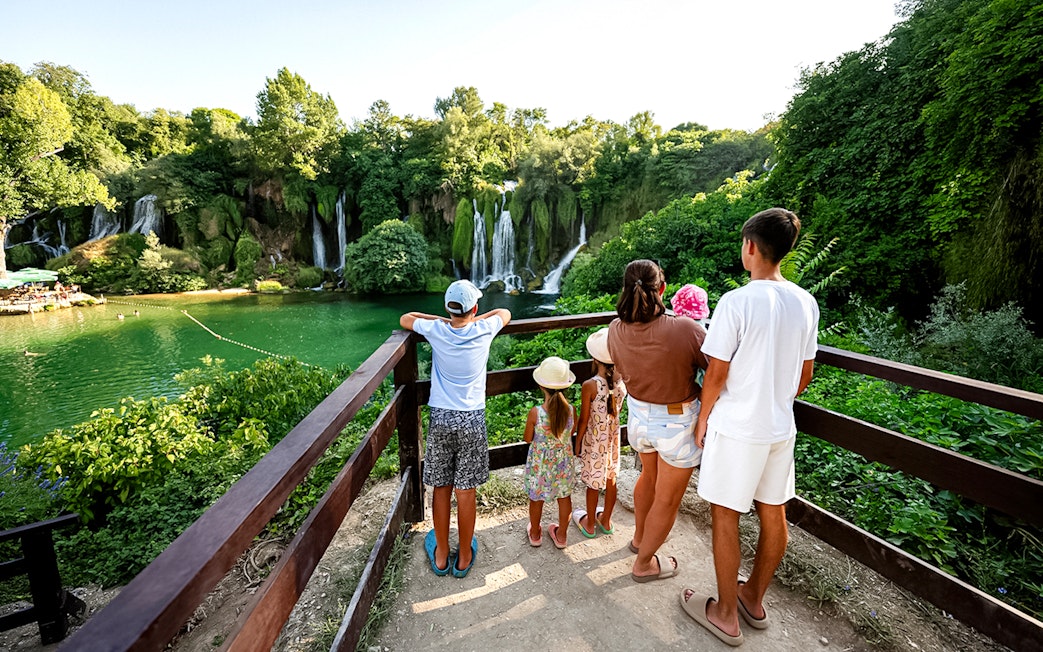 Guests viewing Kravica Waterfalls from a wooden platform surrounded by lush greenery.