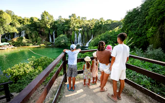 Guests viewing Kravica Waterfalls from a wooden platform surrounded by lush greenery.