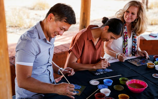 People painting Aboriginal art during Uluru sunrise tour with refreshments.
