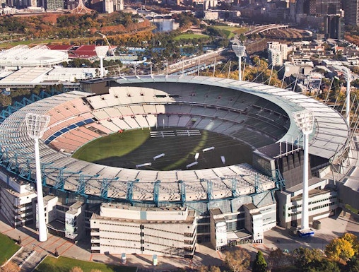 Aerial view of Melbourne Cricket Ground with city skyline in the background.