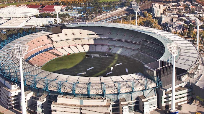 Aerial view of Melbourne Cricket Ground with city skyline in the background.