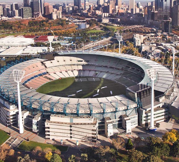 Aerial view of Melbourne Cricket Ground with city skyline in the background.