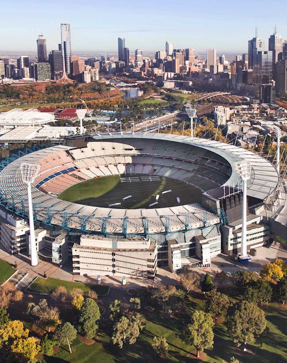 Aerial view of Melbourne Cricket Ground with city skyline in the background.
