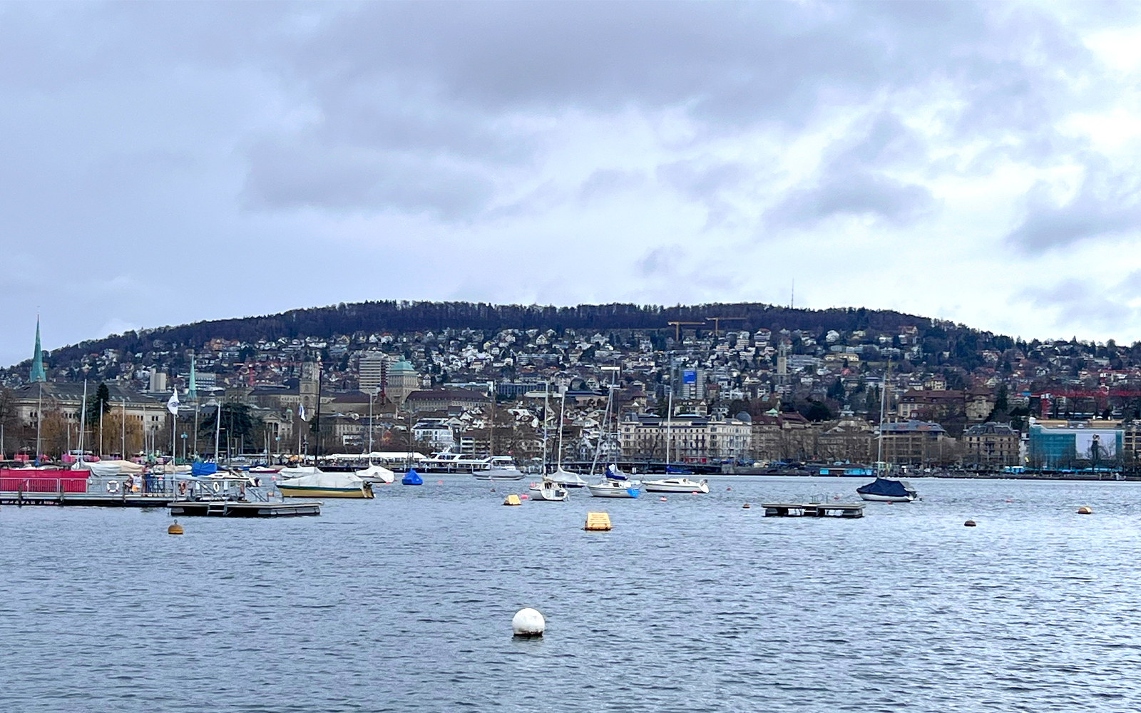 Boats on Lake Zurich with cityscape and hills in the background, view from sightseeing cruise.