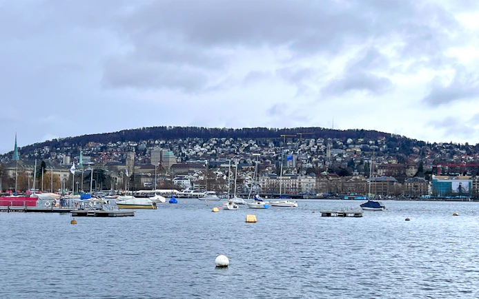 Boats on Lake Zurich with cityscape and hills in the background, view from sightseeing cruise.