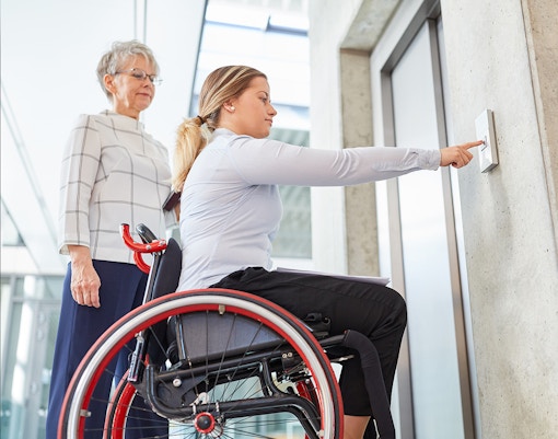 Wheelchair user pressing elevator button for disabled access.