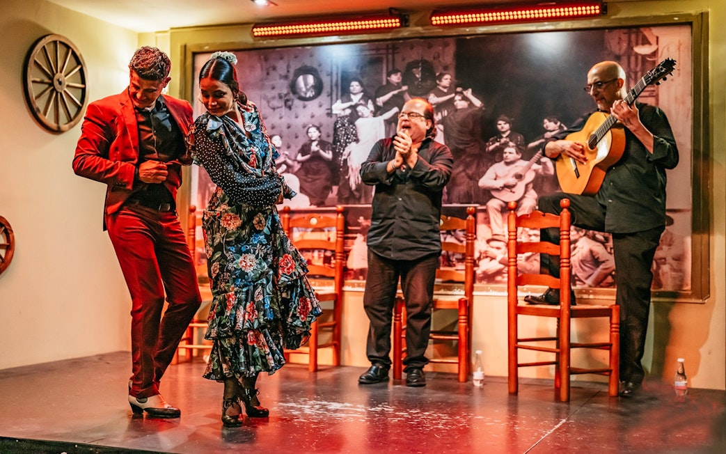 Flamenco dancers performing on stage with guitarist and clapping audience, Spain.