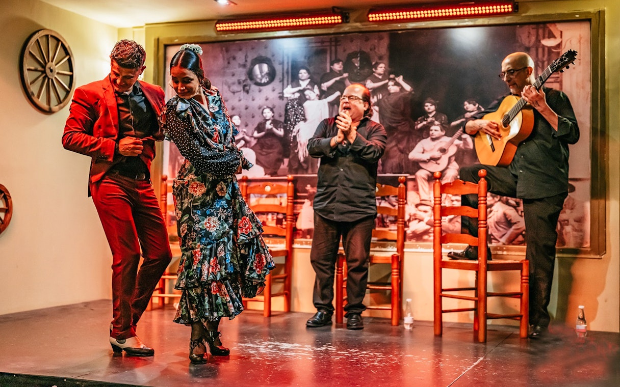 Flamenco dancers performing on stage with guitarist and clapping audience, Spain.