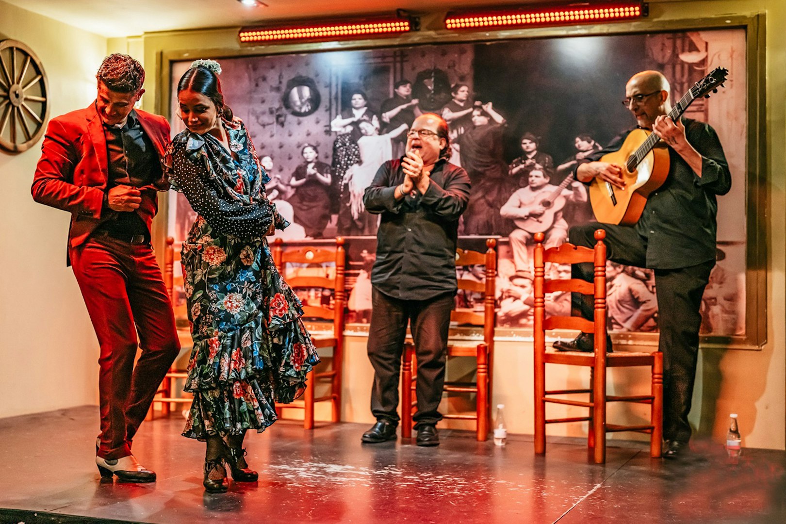 Flamenco dancers performing on stage with guitarist and clapping audience, Spain.