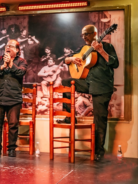 Flamenco dancers performing on stage with guitarist and clapping audience, Spain.