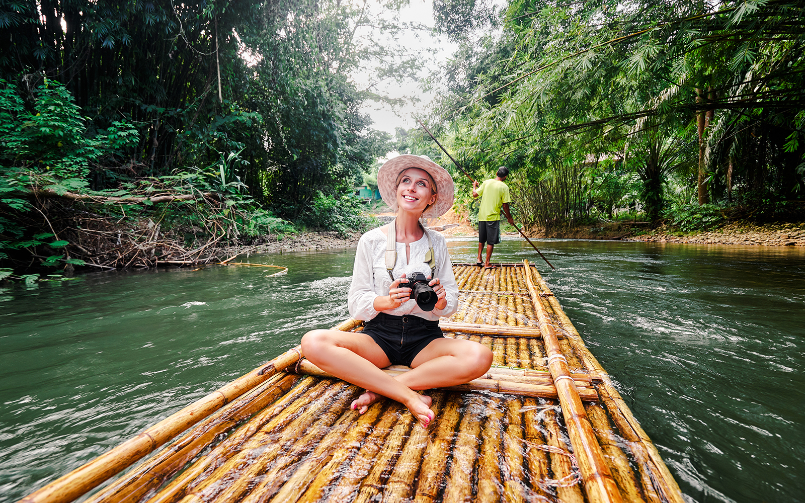 Woman on bamboo raft enjoying jungle river view.