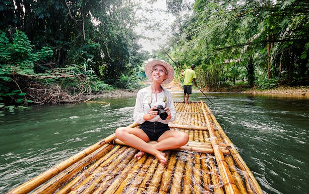 Woman on bamboo raft enjoying jungle river view.