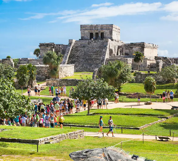 Iguana on ancient Tulum ruins with tourists in Mexico.