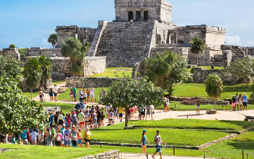 Iguana on ancient Tulum ruins with tourists in Mexico.