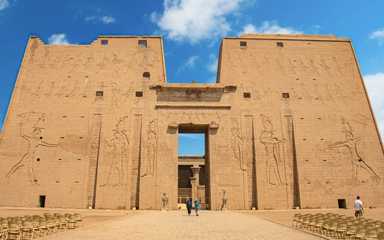 Visitors entering the Temple of Horus at Edfu, Egypt, with ancient carvings on the facade.