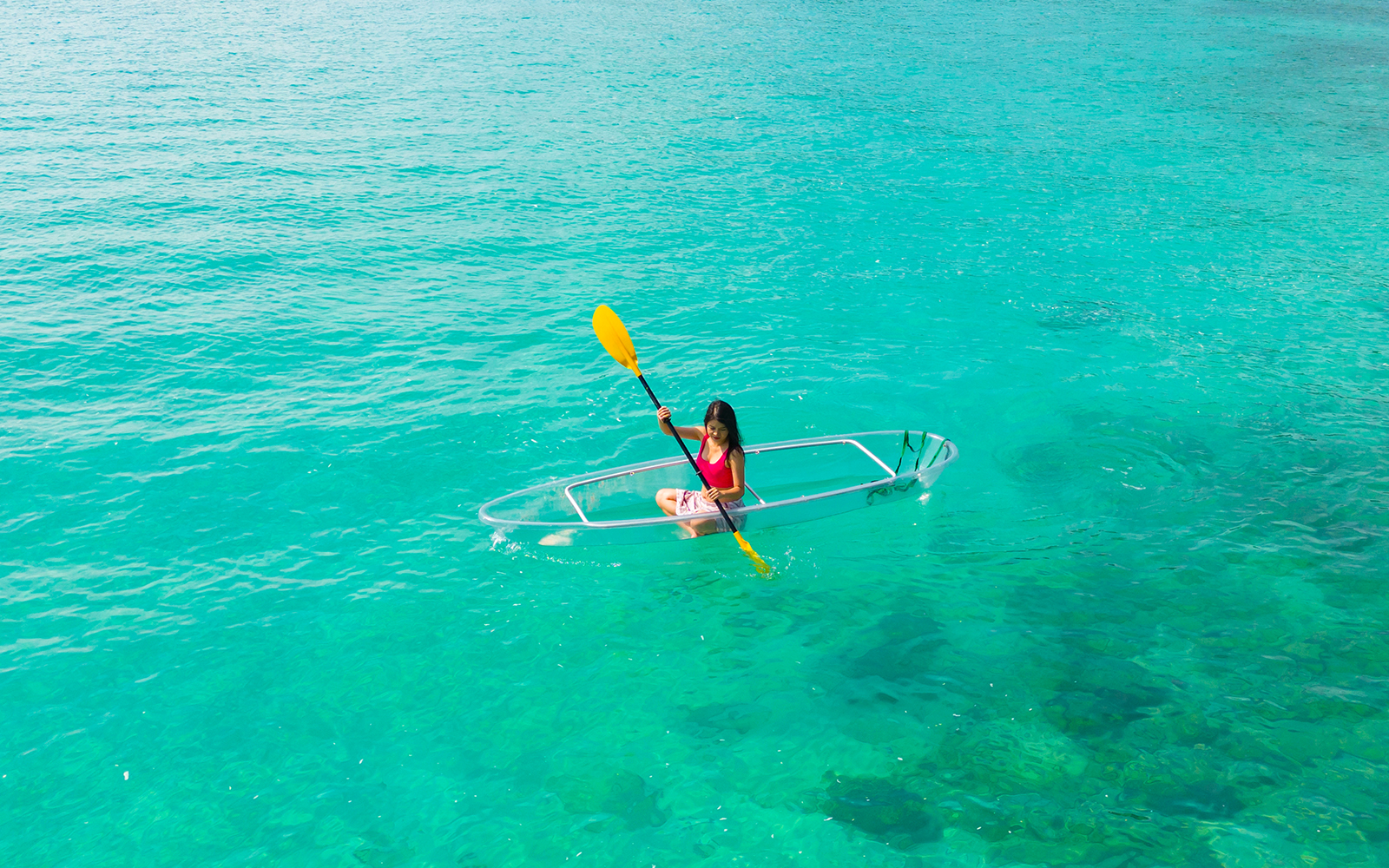 Woman kayaking in a glass-bottom kayak on clear turquoise water.
