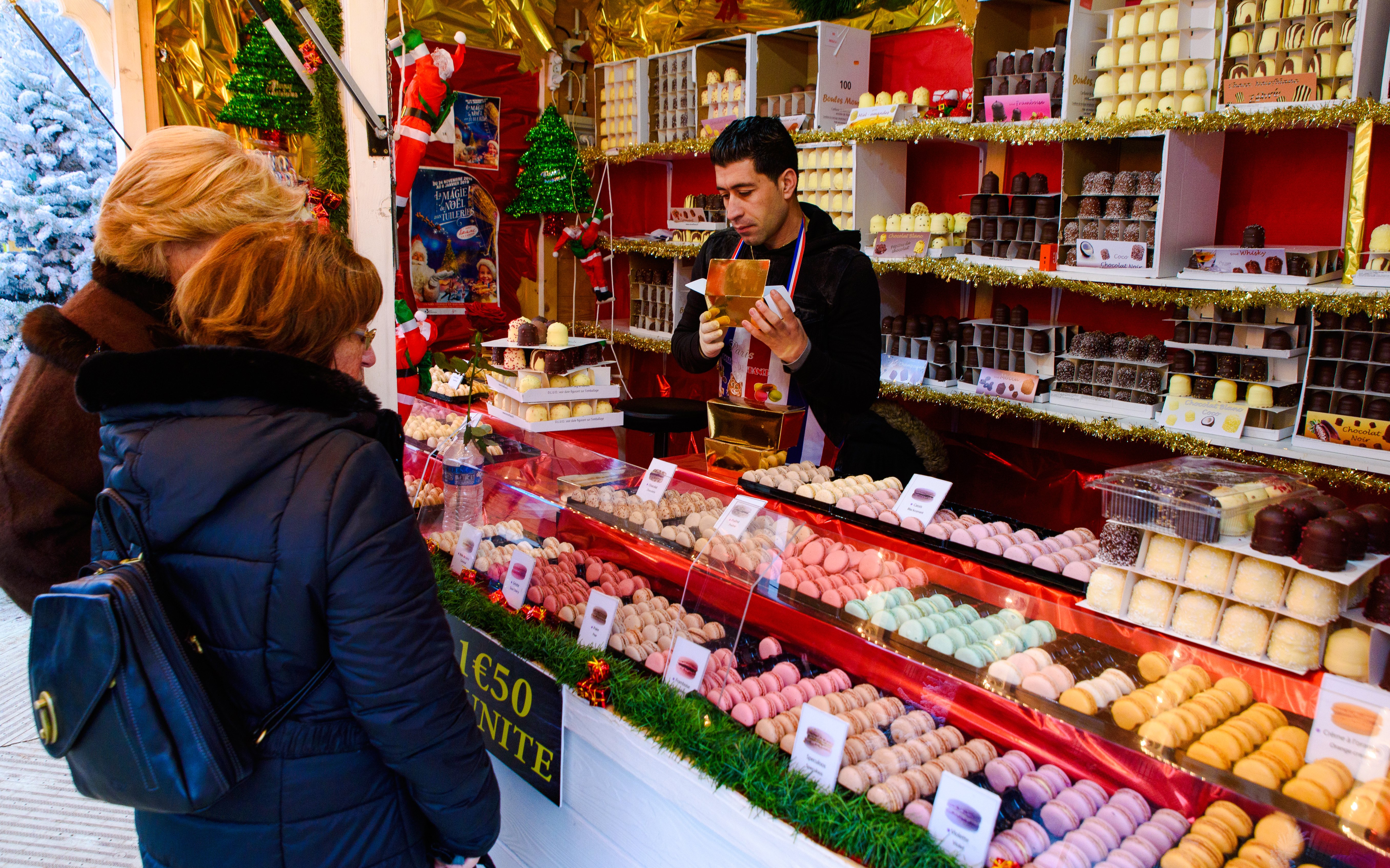 Vendor selling chocolates at Paris Christmas market with women browsing.