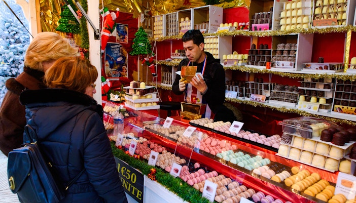 Vendor selling chocolates at Paris Christmas market with women browsing.