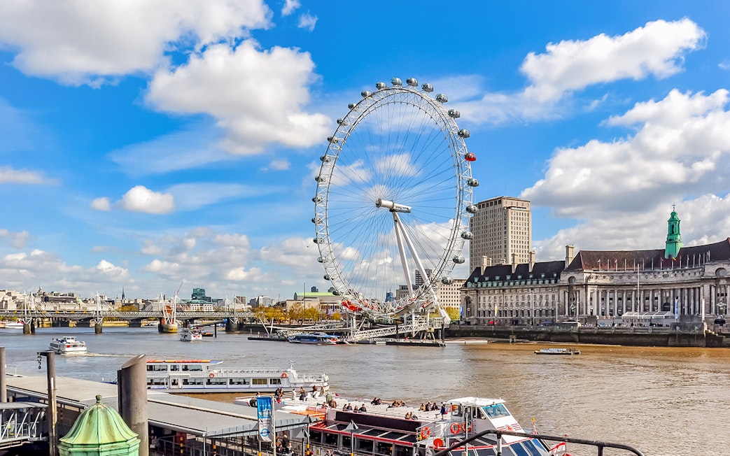 Tourists on a boat near the London Eye with city skyline in the background.