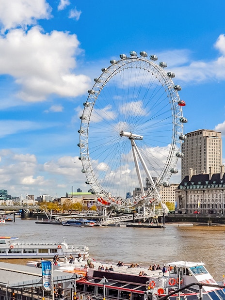 Tourists on a boat near the London Eye with city skyline in the background.
