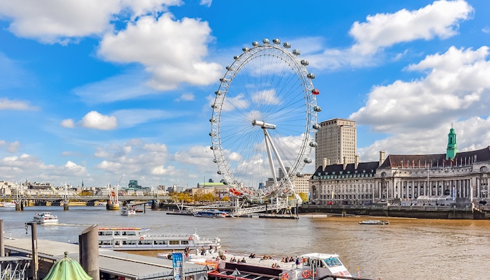 Tourists on a boat near the London Eye with city skyline in the background.