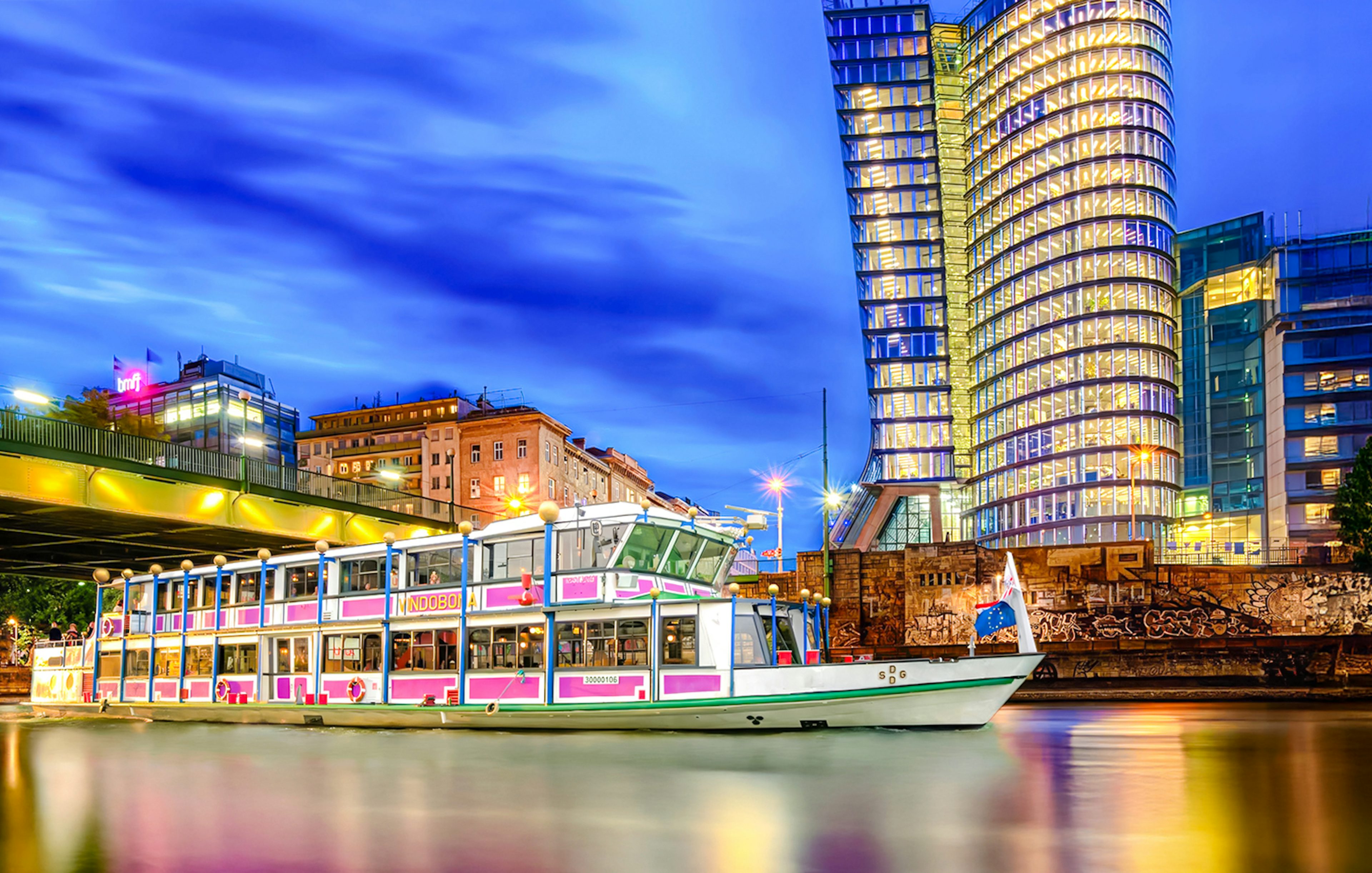 Evening cruise boat on Danube River with illuminated cityscape in the background.
